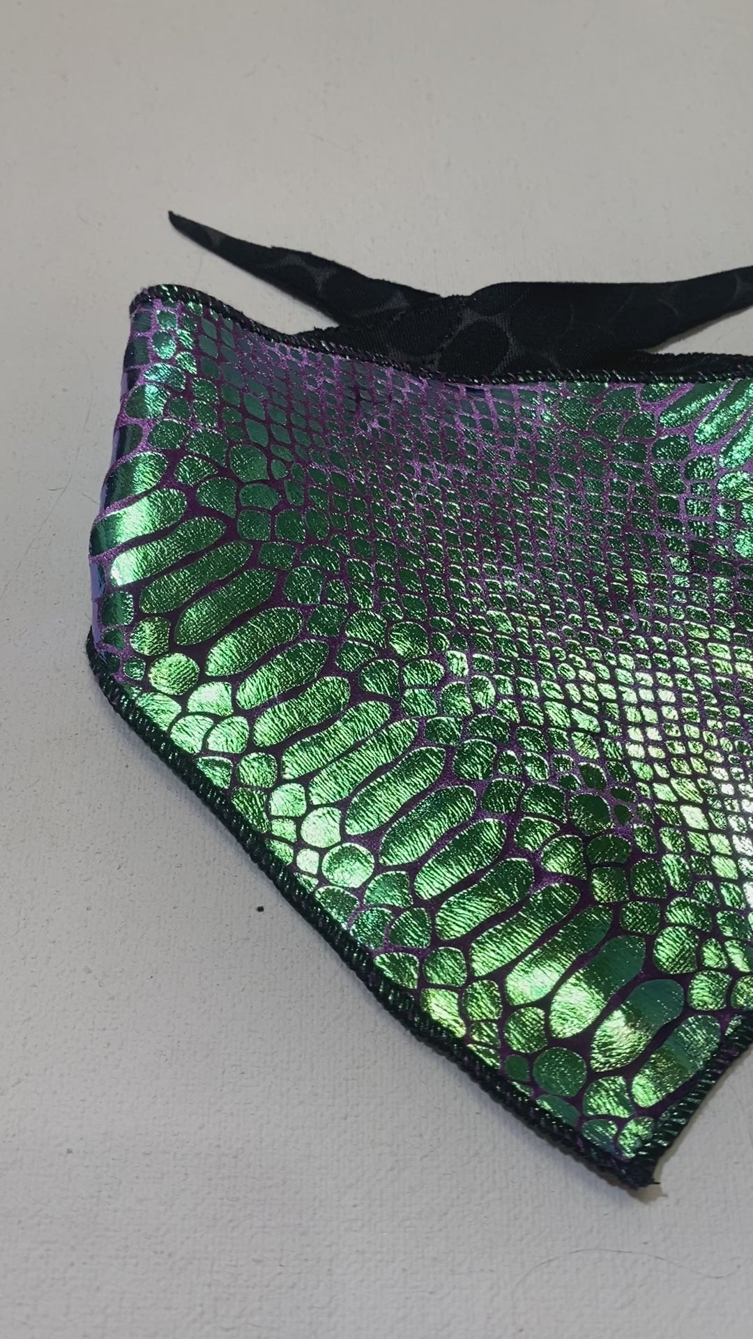 A video of a green and purple velvet snake skin pattern bandana with a shiny, metallic finish and black ties.